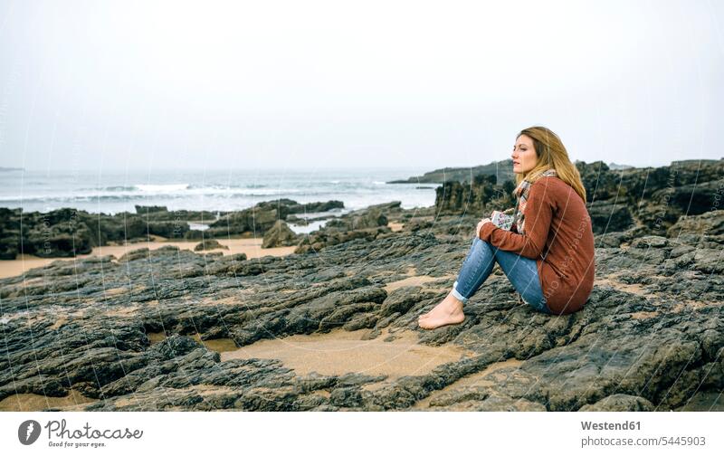 Lonely woman sitting on rocks on the beach in winter Seated females women beaches Adults grown-ups grownups adult people persons human being humans human beings