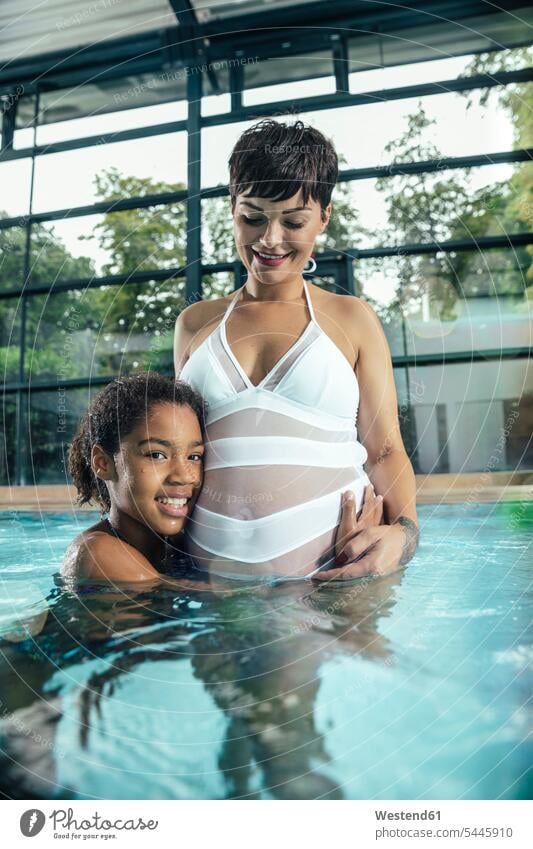 Girl with her pregnant mother in indoor swimming pool indoor swimming pools girl females girls daughter daughters swimming bath mommy mothers mummy mama