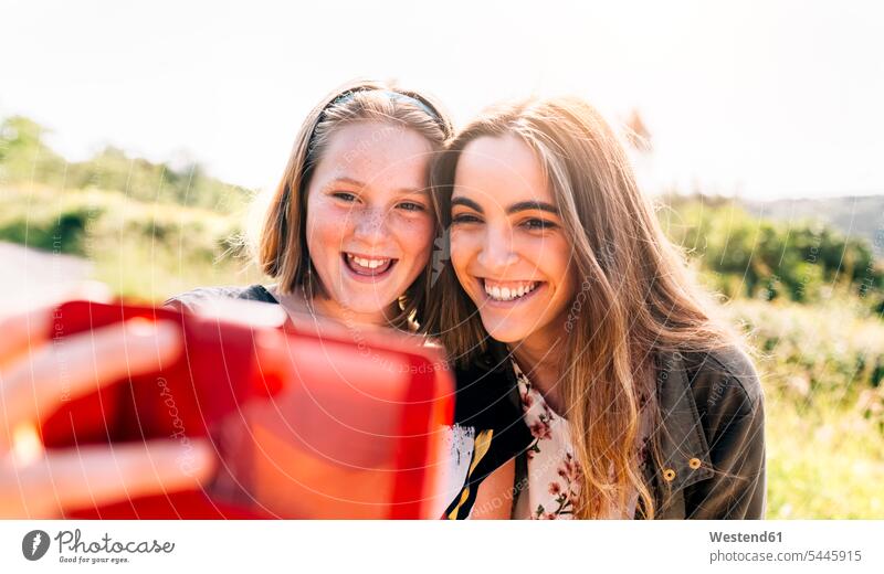 Two happy girls taking a selfie outdoors sister sisters females laughing Laughter portrait portraits happiness Selfie Selfies mobile phone mobiles mobile phones