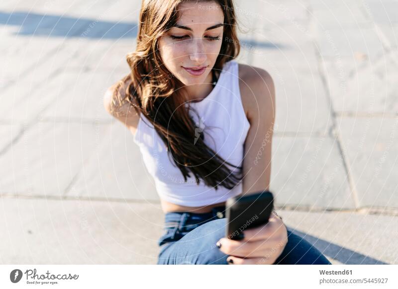 Young woman relaxing on beach promenade looking at cell phone females women Smartphone iPhone Smartphones Adults grown-ups grownups adult people persons