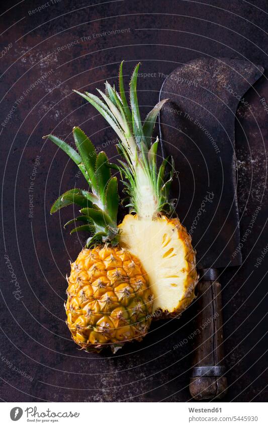 Sliced baby pineapple and old cleaver on rusty metal rusting rusted metals copy space healthy eating nutrition half halves halved sliced dark background