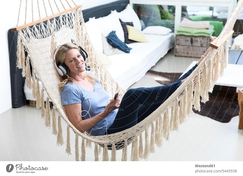 Relaxed woman at home lying in hammock listening to music relaxed relaxation headphones headset hammocks females women smiling smile laying down lie lying down