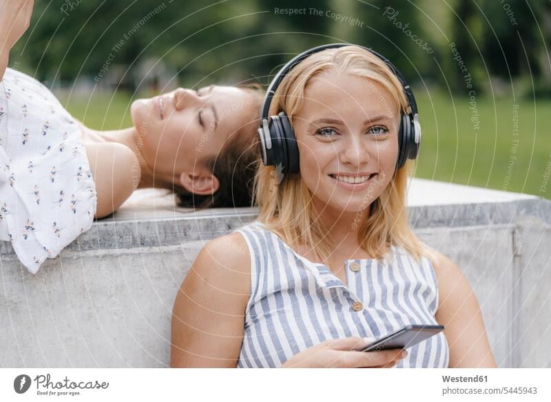 Portrait of young woman with cell phone and headphones in a skatepark mobile phone mobiles mobile phones Cellphone cell phones headset females women smiling
