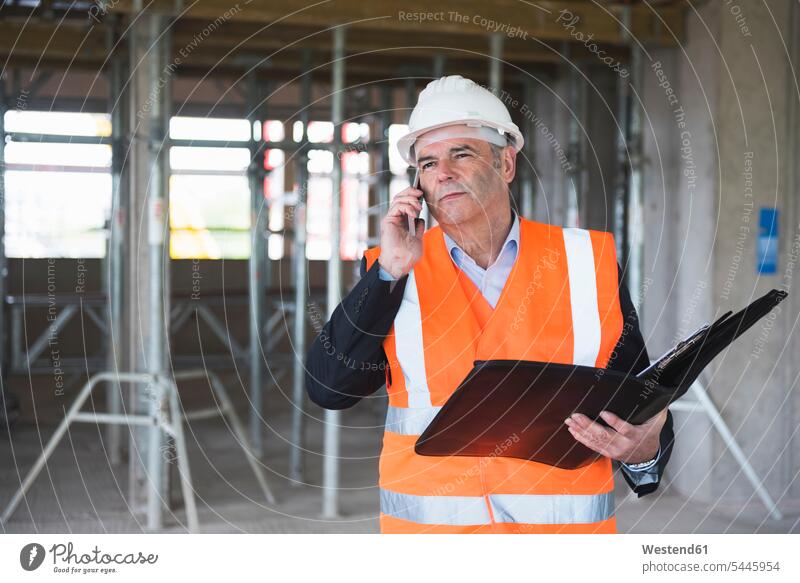 Man on the phone wearing safety vest in building under construction call telephoning On The Telephone calling man men males architect architects