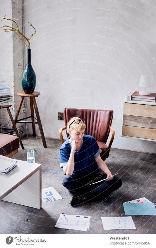 Woman sitting on floot in a loft looking at papers freelancer freelancing woman females women lofts Adults grown-ups grownups adult people persons human being