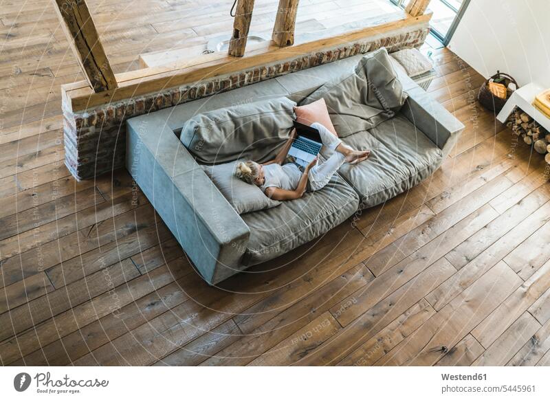 Woman lying on couch, using laptop online cozy sociable comfortable cosy settee sofa sofas couches settees laying down lie lying down woman females women