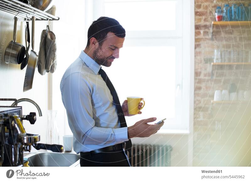 Businessman having coffee break in office kitchen looking at cell phone Coffee Business man Businessmen Business men mobile phone mobiles mobile phones