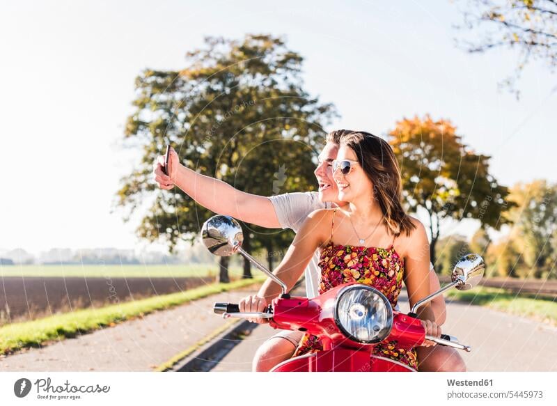 Happy young couple taking a selfie on motor scooter on country road Selfie Selfies motor-scooter rural road rural roads country roads twosomes partnership