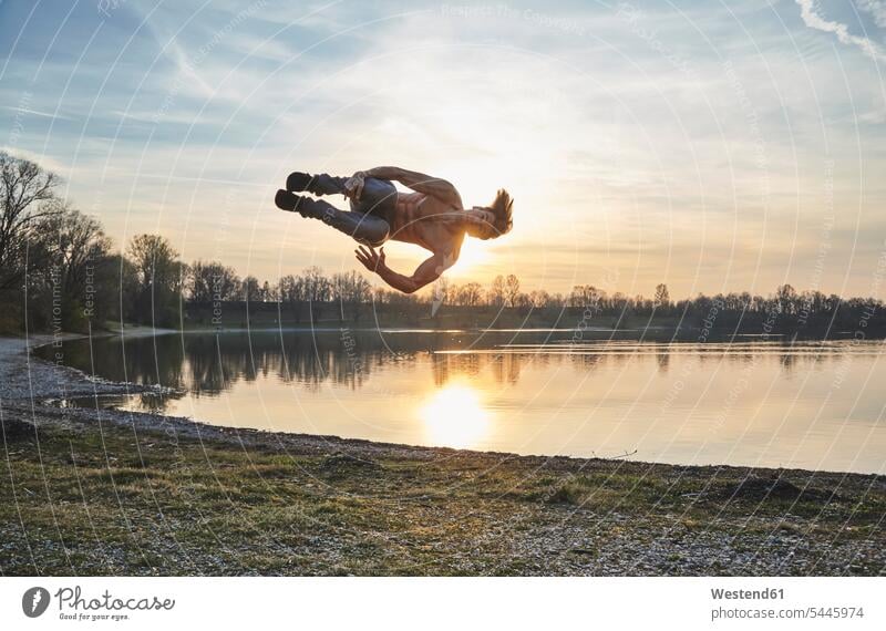 Germany, Bavaria, Feldkirchen, man doing parkour at lakeshore jumping Leaping Parcour men males water waters body of water jumps Adults grown-ups grownups adult