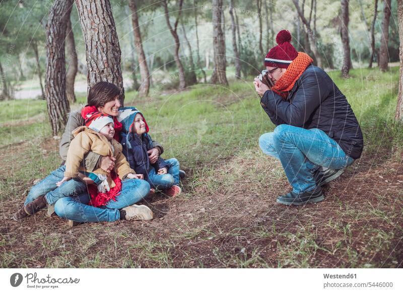 Father taking a picture of his family in forest happiness happy smiling smile photographing families boy boys males people persons human being humans
