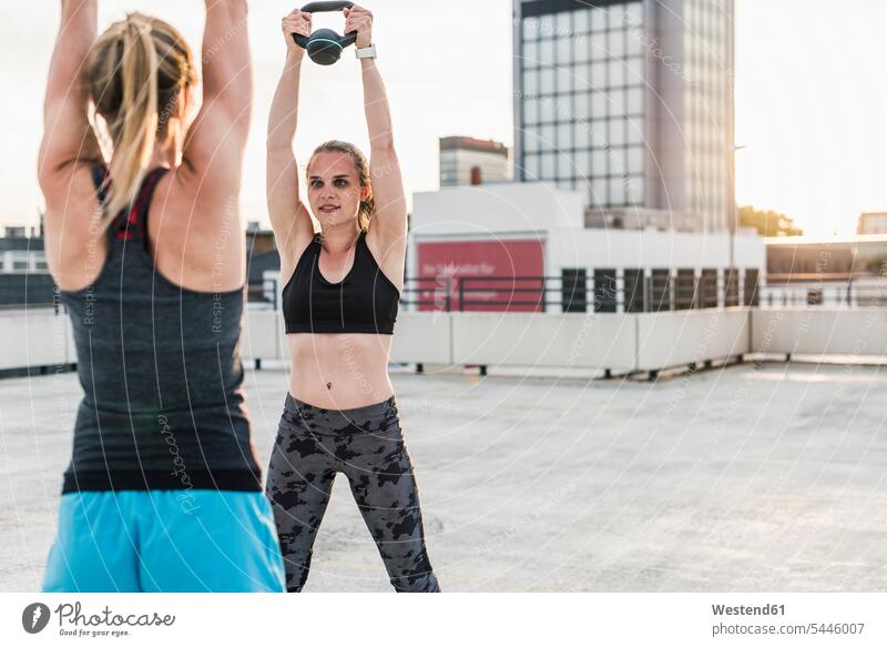 Two women exercising with kettlebells on parking level in the city weight lifting exercise training practising woman females Adults grown-ups grownups adult