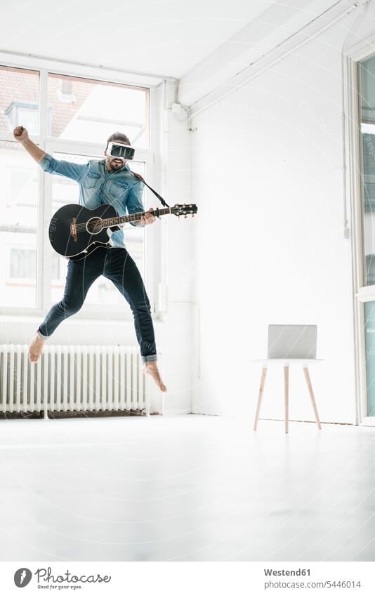 Man with guitar wearing Virtual Reality Glasses jumping in the air in a loft man men males guitars jump in the air VR glasses Virtual-Reality Glasses