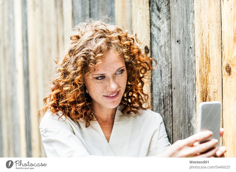 Portrait of smiling young woman taking selfie with cell phone in front of wooden wall Selfie Selfies portrait portraits females women Adults grown-ups grownups