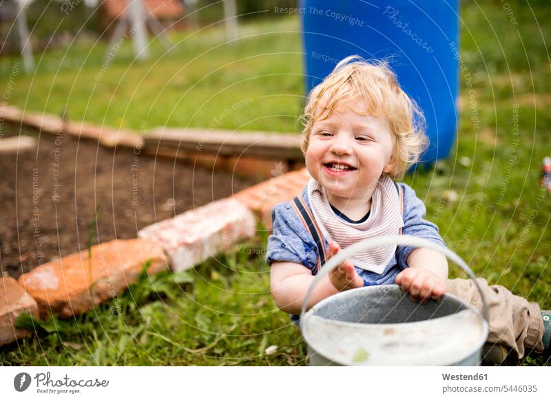 Boy in garden playing with watering can smiling smile gardens domestic garden watering cans casual leisure wear casual clothing casual wear casual clothes