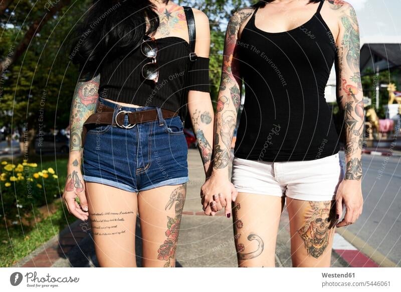 Tattooed lesbian couple holding hands in the street in summer tattoo tattoos woman females women twosomes partnership couples tattooed body art Body Adornment