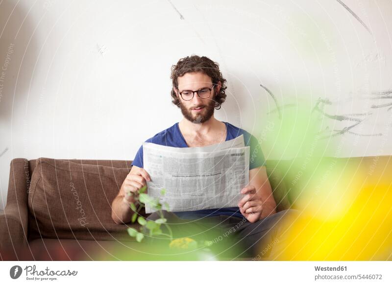 Portrait of young man reading newspaper on couch in a coffee shop men males newspapers portrait portraits Adults grown-ups grownups adult people persons