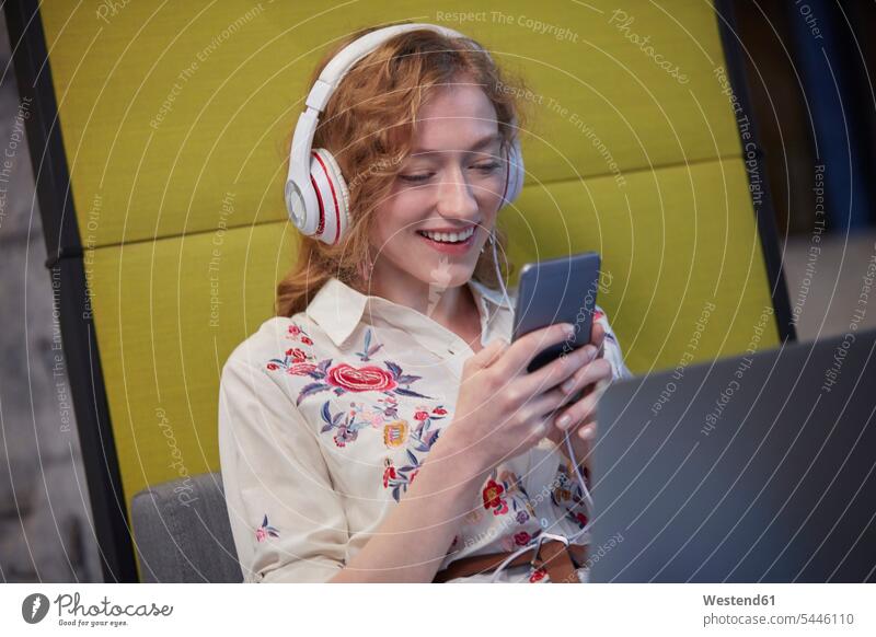 Young woman working in modern creative office, wearing headphones, using smartphone offices office room office rooms At Work on the phone call telephoning