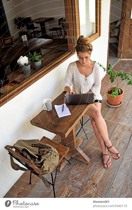 Young woman sitting on veranda of a coffee shop using laptop Laptop Computers laptops notebook females women computer computers Adults grown-ups grownups adult