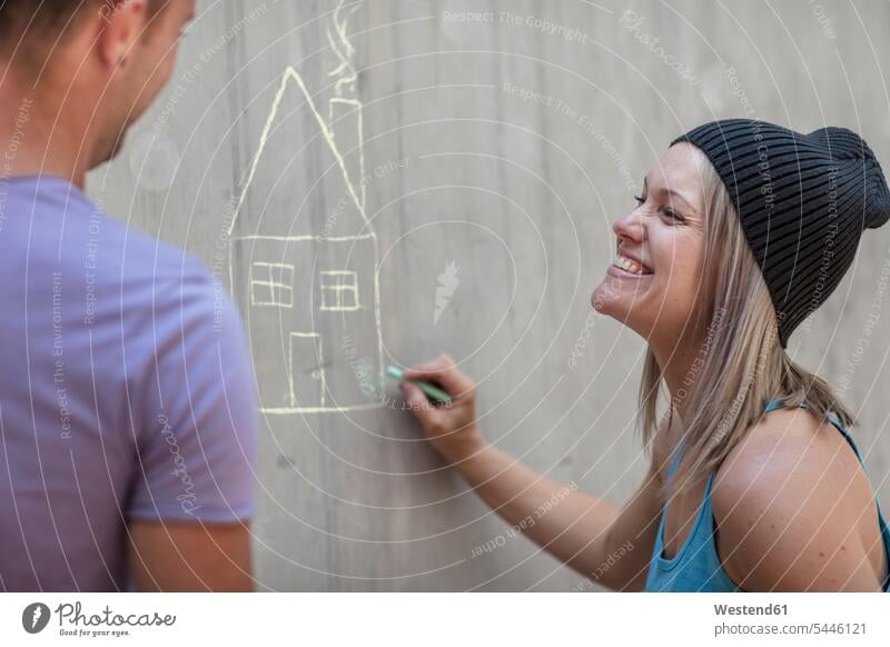 Man and woman drawing a house with chalk on concrete wall men males females women concrete walls sketching houses Adults grown-ups grownups adult people persons