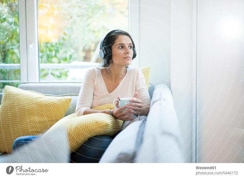 Woman sitting alone on couch, listening music with headphones Listening Music Seated headset solitary solo settee sofa sofas couches settees Coffee copy space