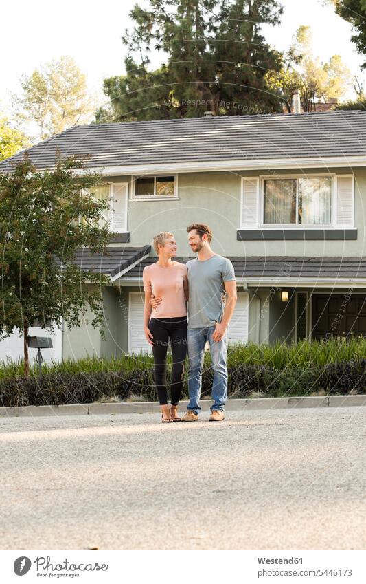 Smiling couple standing in front of their home twosomes partnership couples smiling smile house houses people persons human being humans human beings building