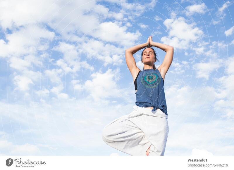 Woman doing a yoga exercise under sky with clouds exercises Yoga woman females women Adults grown-ups grownups adult people persons human being humans