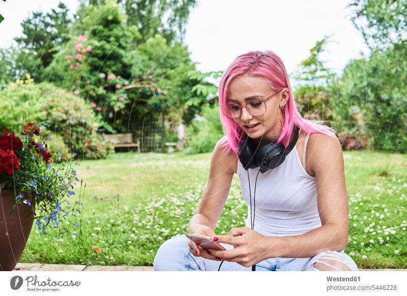 Young woman with pink hair wearing headphones and using cell phone in garden mobile phone mobiles mobile phones Cellphone cell phones gardens domestic garden