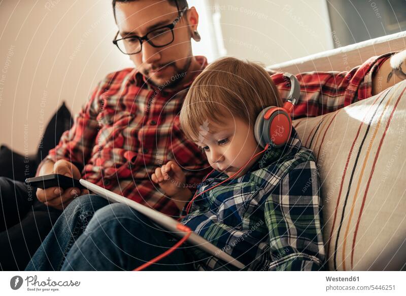 Father and son on couch using tablet and wearing headphones sons manchild manchildren headset father pa fathers daddy dads papa digitizer Tablet Computer