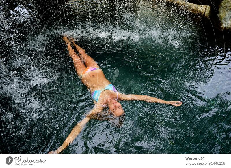Young woman floating in water in pool with waterfall females women Adults grown-ups grownups adult people persons human being humans human beings vacation