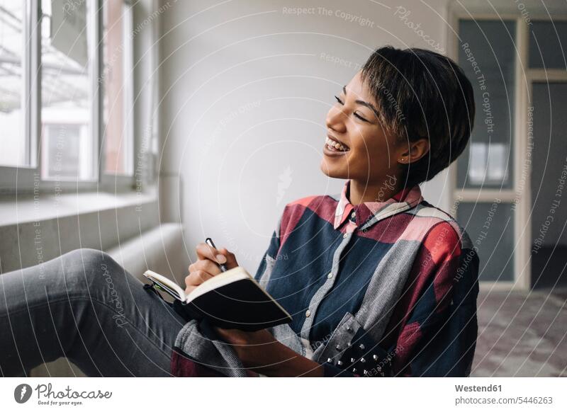 Smiling woman sitting at the window with notebook smiling smile businesswoman businesswomen business woman business women writing write females notebooks