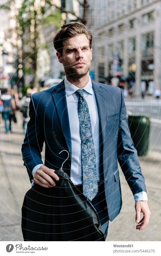 Handsome businessman walking in Manhattan, carrying jacket on a hanger coat coats jackets commuter commuters going Businessman Business man Businessmen