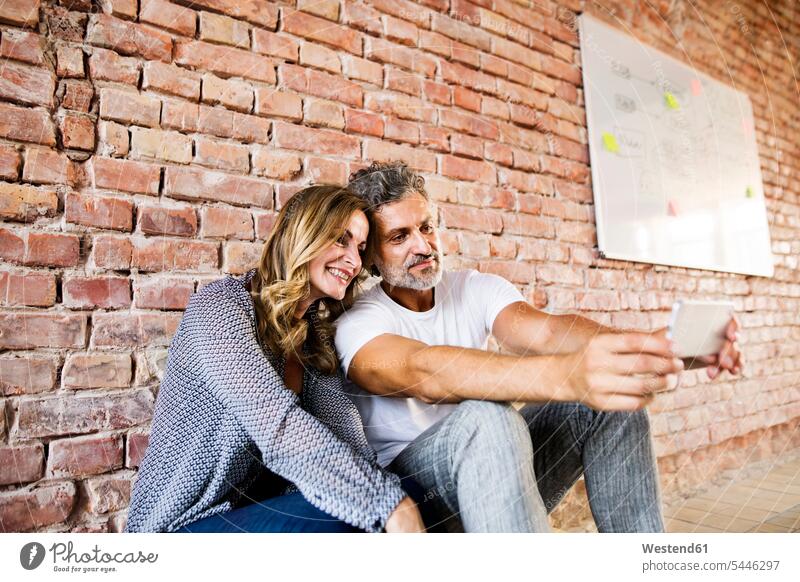 Businessman and woman sitting in their new office, sharing selfies loft lofts Seated startup young business start up startup company startups young company
