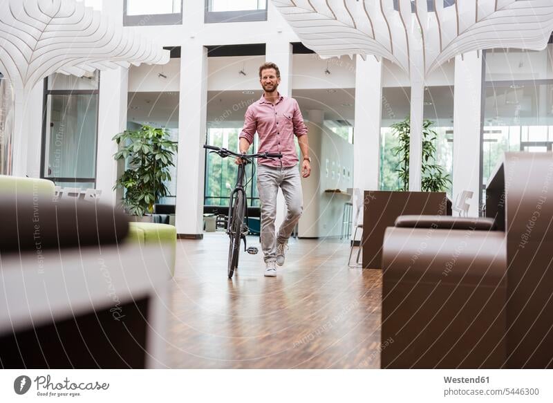 Man with bicycle walking in office bikes bicycles going smiling smile man men males Adults grown-ups grownups adult people persons human being humans