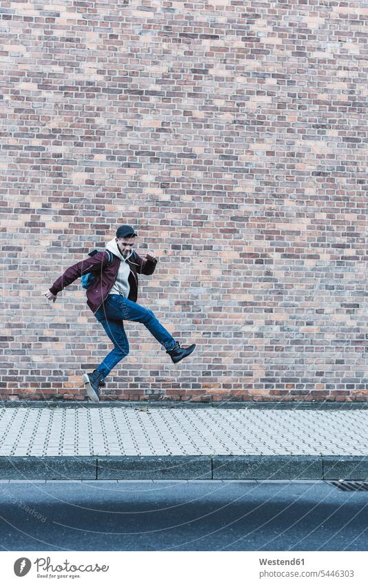 Young man jumping in front of brick wall men males Leaping Adults grown-ups grownups adult people persons human being humans human beings jumps pavement