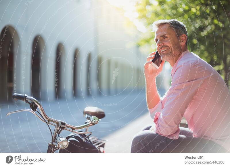 Smiling man with bicycle on the phone on a park bench bikes bicycles parks sitting Seated smiling smile benches men males call telephoning On The Telephone