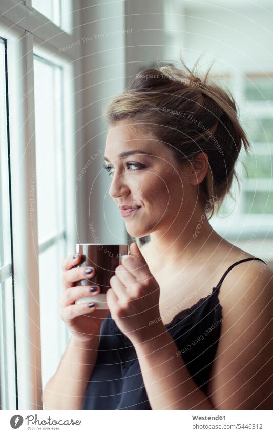 Portrait of smiling blond woman with glass of coffee looking through window females women portrait portraits Adults grown-ups grownups adult people persons