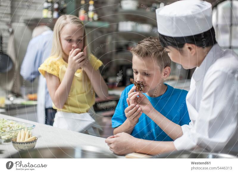 Boy and girl smelling food from female chef in cooking class kitchen female cook cooks Chefs kitchen counter countertops kitchen counters Kitchen Worktop