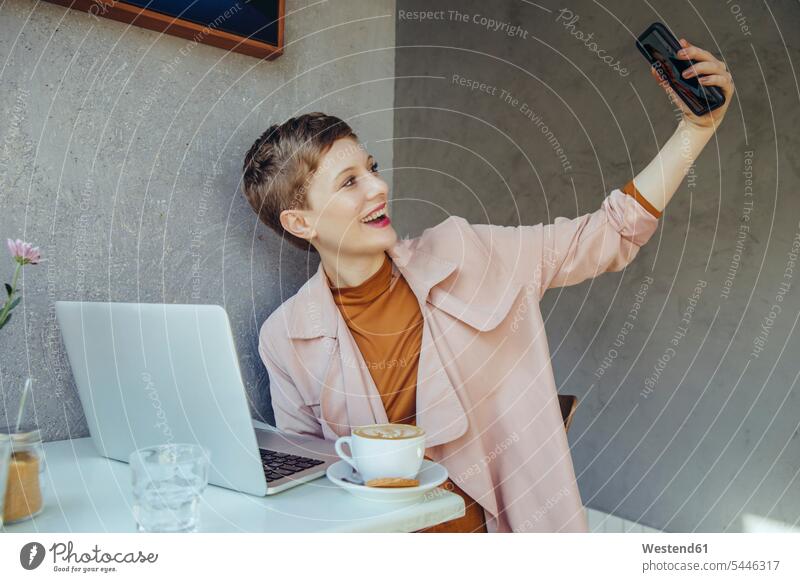 Woman taking a selfie with her laptop in a cafe mobile phone mobiles mobile phones Cellphone cell phone cell phones Selfie Selfies Laptop Computers laptops