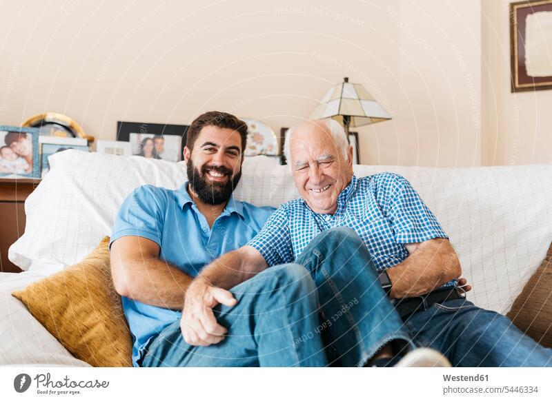 Portrait of adult grandson and his grandfather sitting on the couch at home tickling each other grandsons grandpas granddads grandfathers grandchild