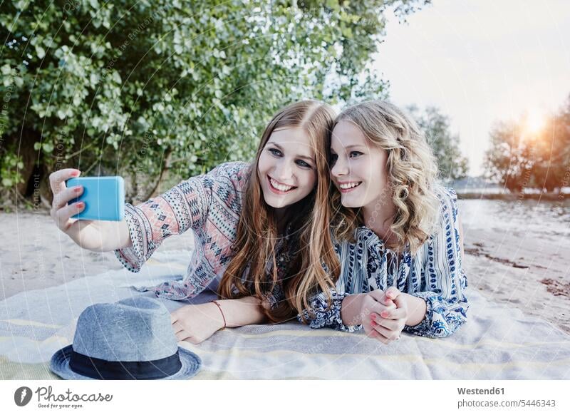Two teenage girls lying on blanket on the beach taking selfie female friends Selfie Selfies mate friendship laying down lie lying down Smartphone iPhone