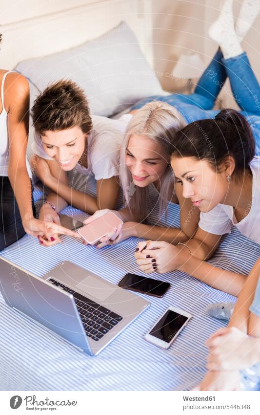 Happy female friends sharing laptop in bedroom beds home at home happiness happy Laptop Computers laptops notebook woman females women Domestic Bedroom mate