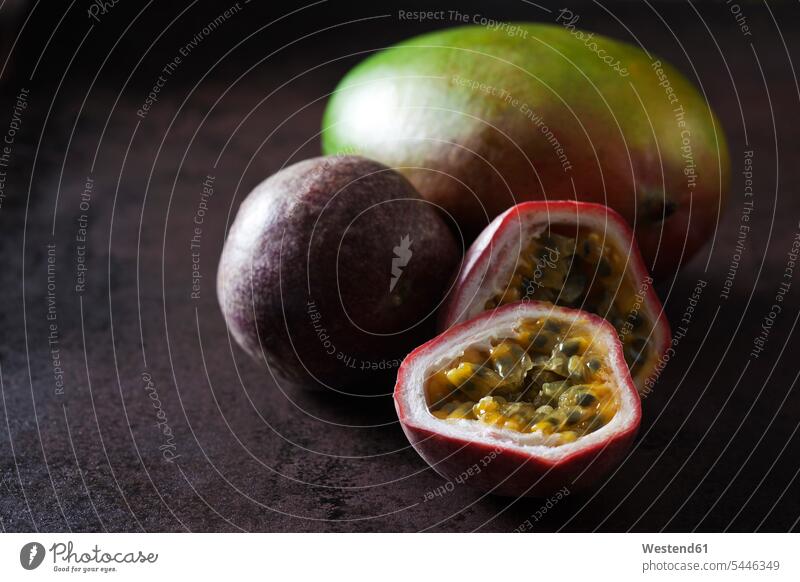 Whole and sliced passion fruit and a mango, on dark ground nobody whole half halves halved healthy eating nutrition copy space focus on foreground