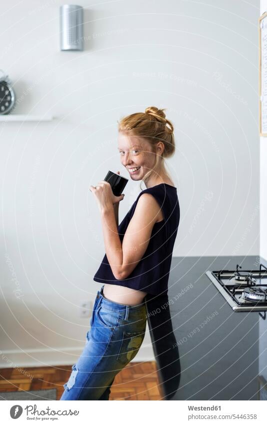Young woman standing in kitchen, drinking coffee Coffee young women young woman blond blond hair blonde hair home at home redheaded red hair red hairs