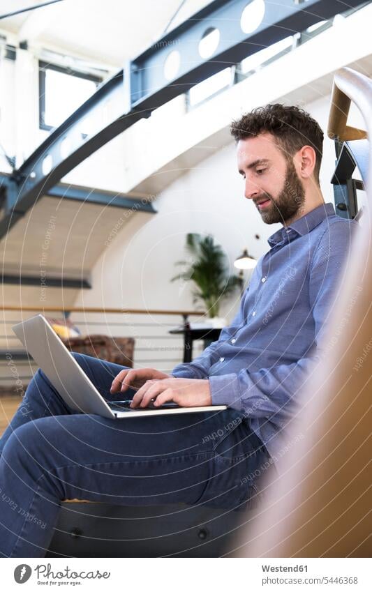 Man sitting on floor using laptop in modern office man men males Laptop Computers laptops notebook Seated offices office room office rooms Adults grown-ups