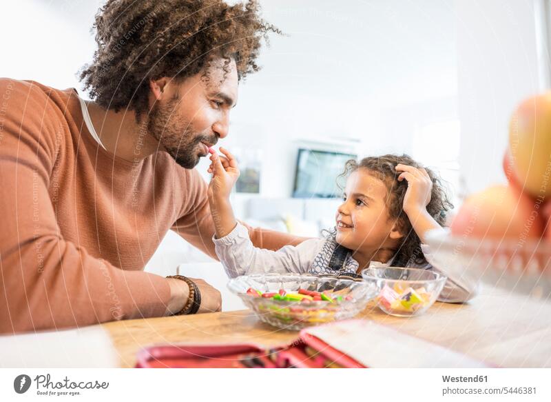 Smiling girl feeding father at home with sweets nibbling snacking nibble Care caring care females girls smiling smile pa fathers daddy dads papa eating child
