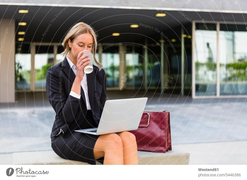 Businesswoman with fashionable leatherbag and coffee to go sitting on bench looking at laptop businesswoman businesswomen business woman business women drinking