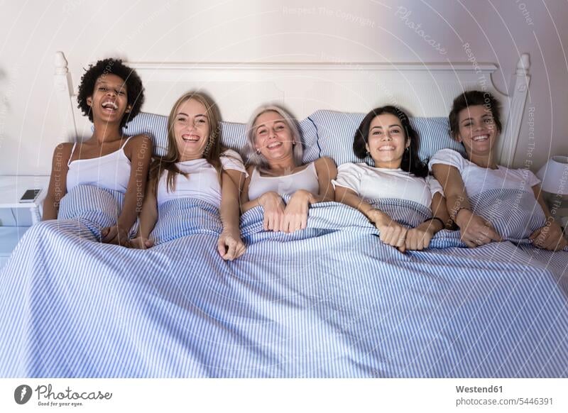 Portrait of happy female friends lying in bed side by side portrait portraits laughing Laughter laying down lie lying down woman females women beds positive
