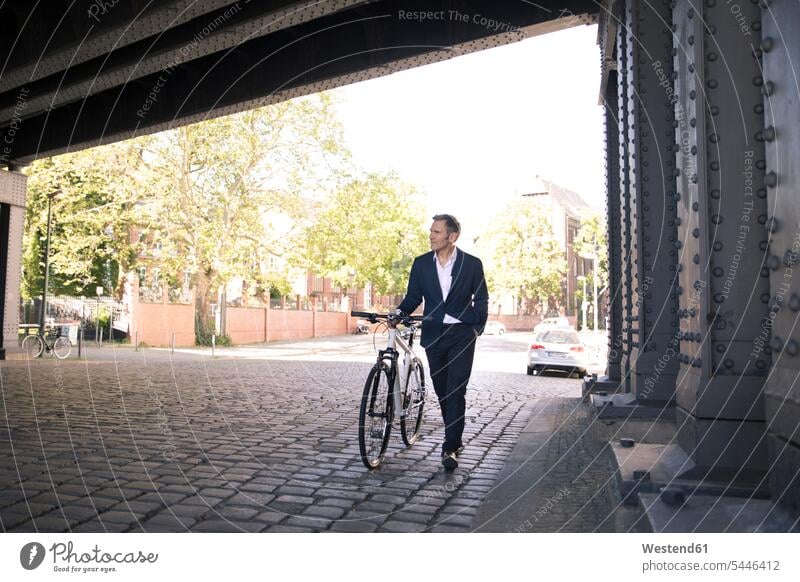 Mature businessman pushing bicycle in the city walking going Businessman Business man Businessmen Business men bikes bicycles town cities towns business people