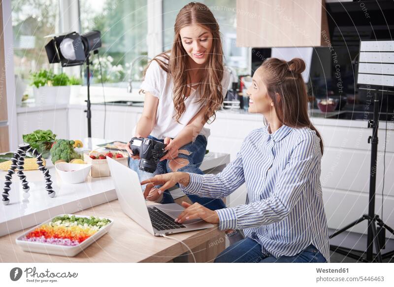 Two food bloggers using laptop and camera in kitchen smile cameras computers Laptop Computer Laptop Computers laptops notebook human human being human beings