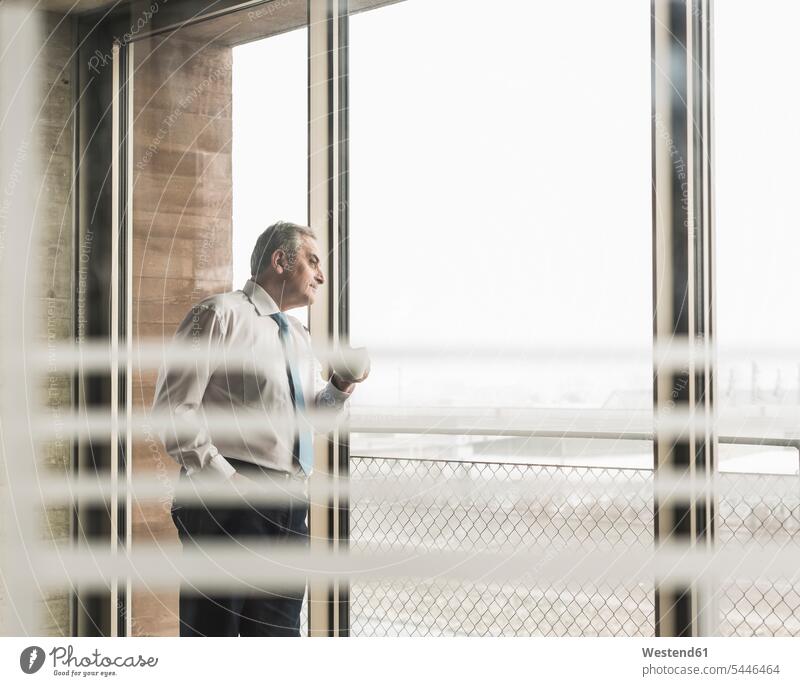 Senior manager in office looking out of window with cup of coffee standing Coffee Businessman Business man Businessmen Business men offices office room